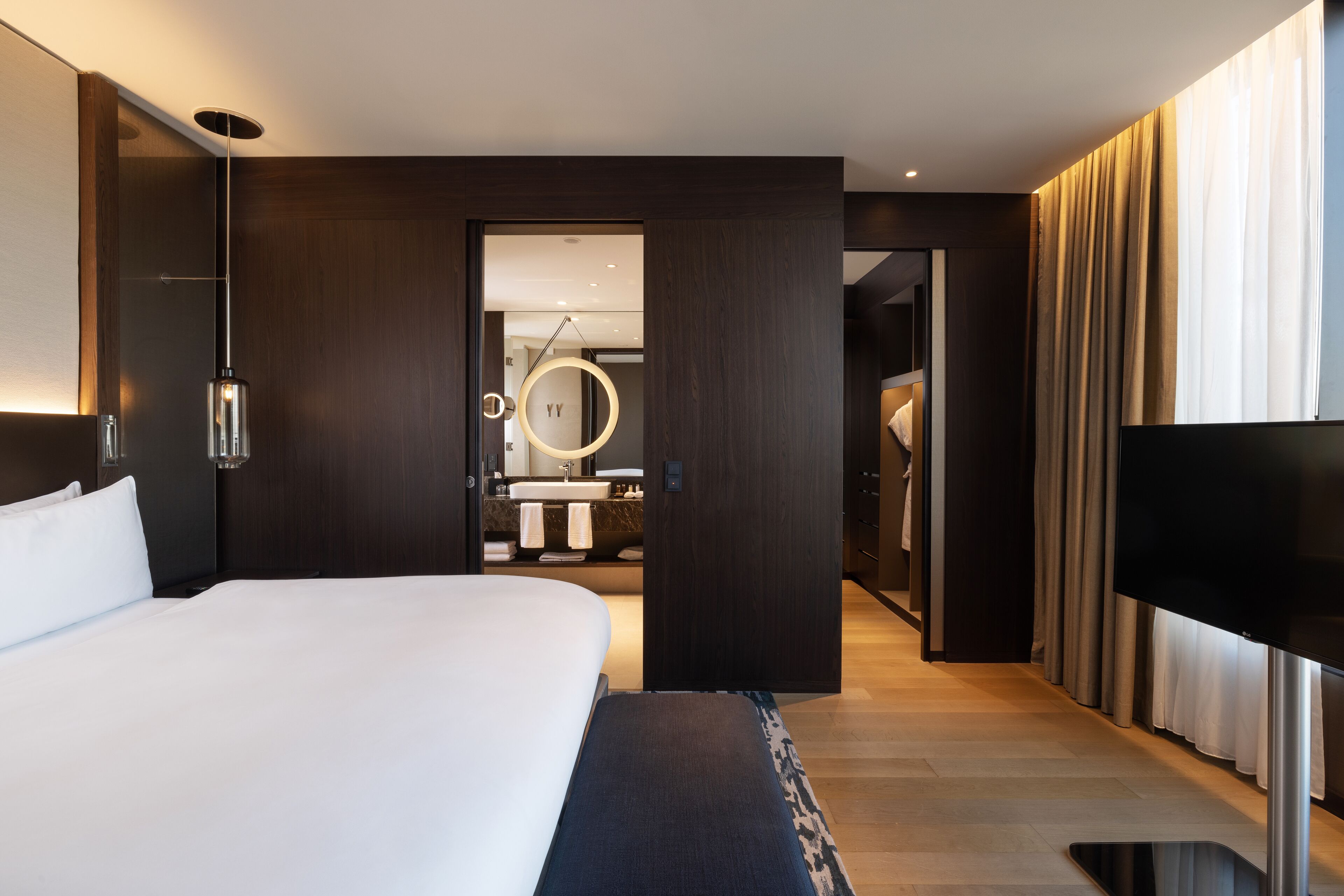Et moderne hotelværelse med en stor seng, et fladskærms-tv og et badeværelse, der kan ses gennem en åben dør.