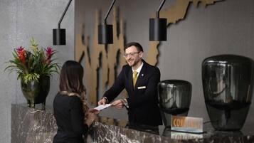 A hotel reception desk with a nameplate, a large vase with flowers, and a modern light fixture.