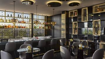 A modern bar with a glass counter, multiple seating areas, and a view of the city through large windows.