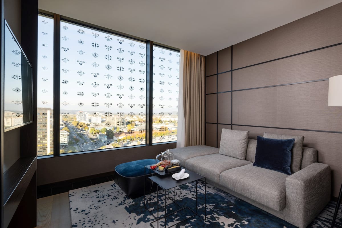 Een moderne hotelkamer met een groot raam, een bank, een bijzettafeltje en een vloerlamp.