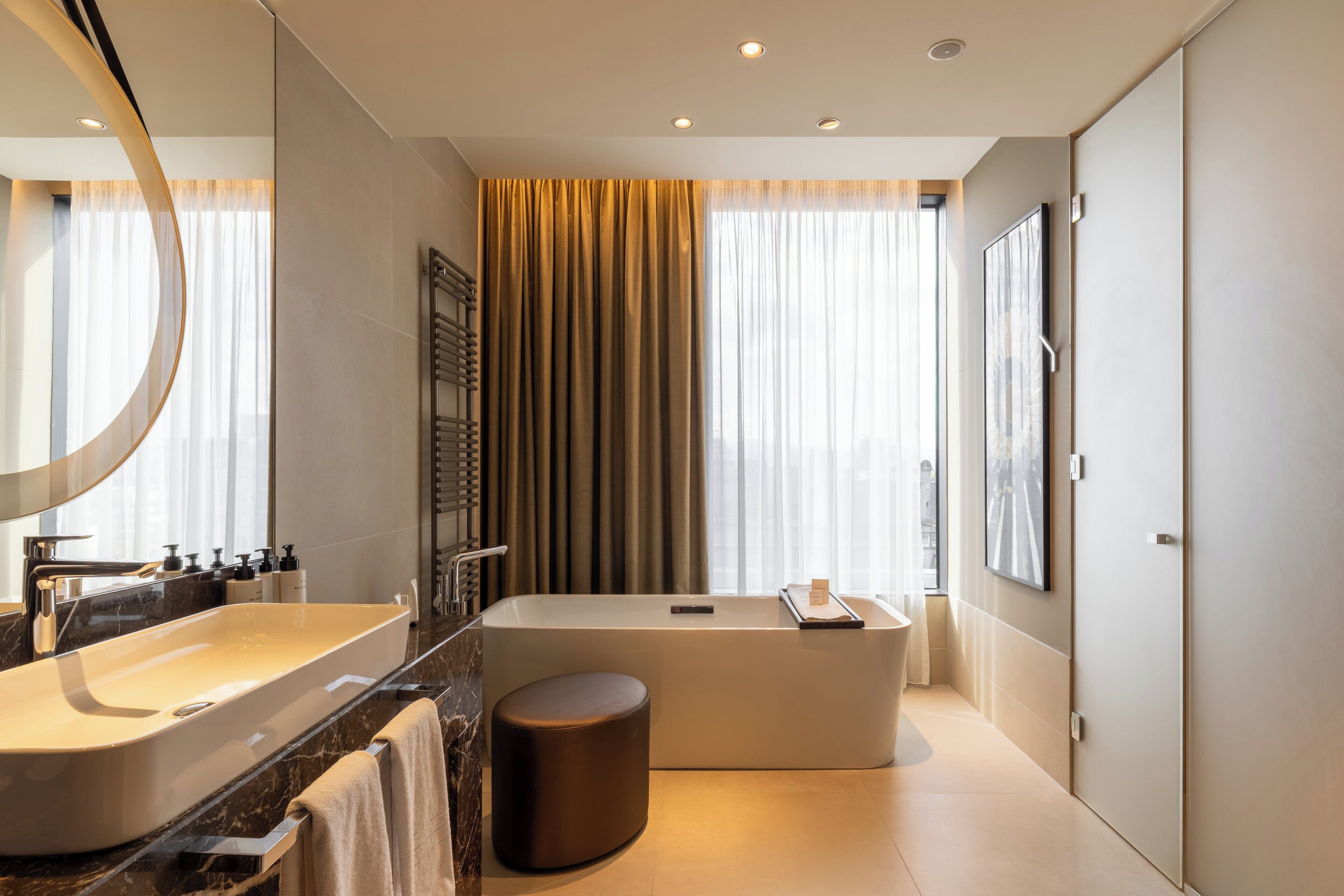 Een moderne badkamer met een groot bad, een wastafel met spiegel en een rond krukje.