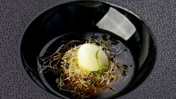 A bowl of food with sprouts and a boiled egg on a dark surface.