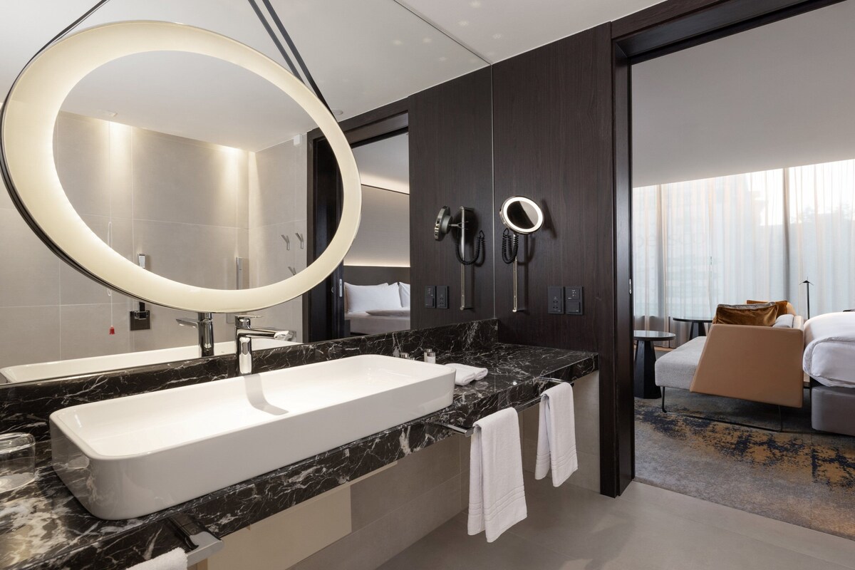Une salle de bain moderne avec un grand miroir ovale, un lavabo blanc et un plan de toilette en marbre.