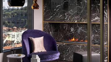 A modern living room with a purple sofa, a fireplace, and a view of a cityscape.