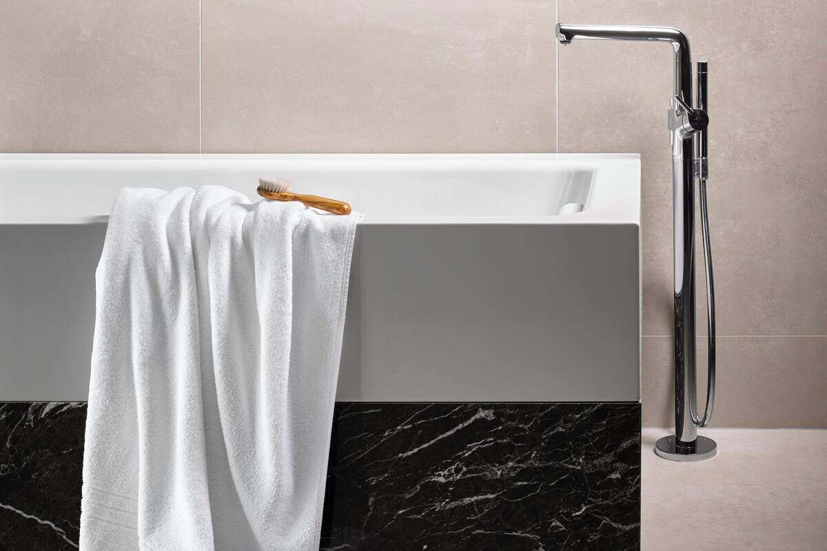 Een moderne badkamer met een groot bad, een douchekraan met houten handgreep, en een handdoek over de badrand.