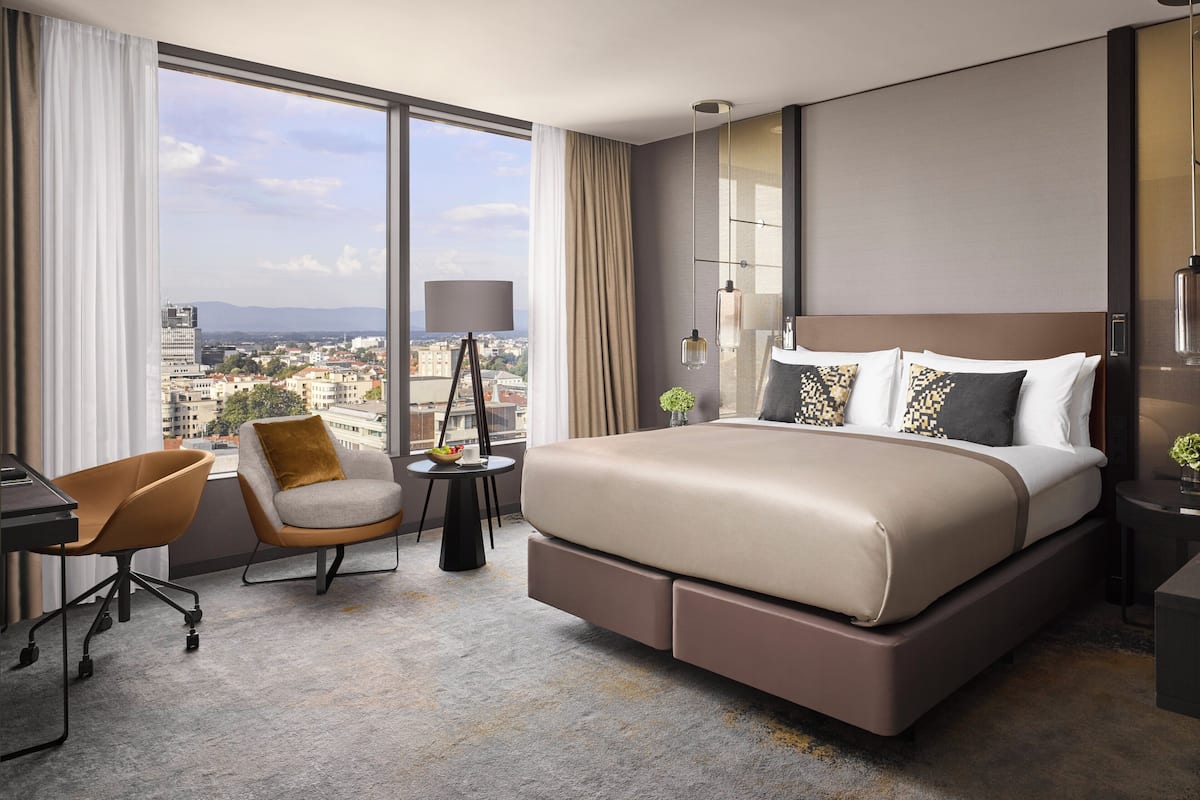 Een moderne hotelkamer met een groot bed, een bureau, een stoel en uitzicht op de stad.