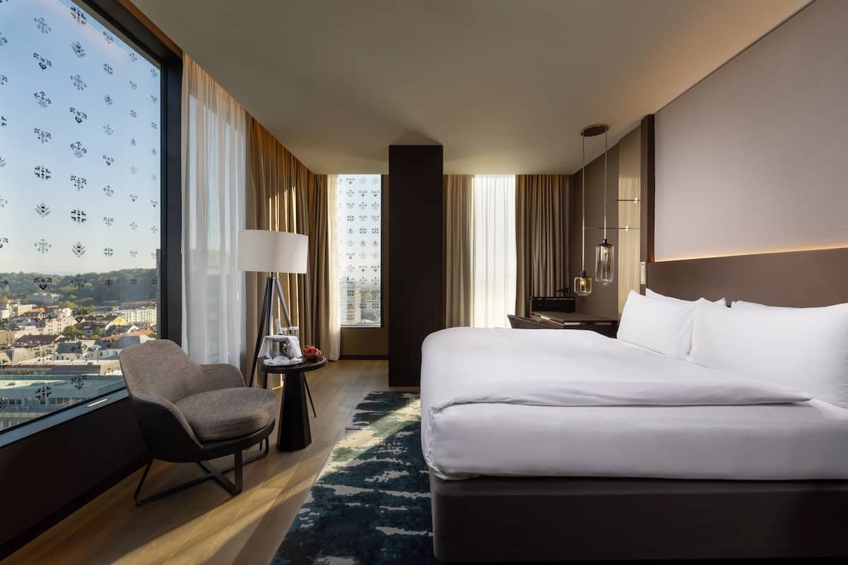 Een hotelkamer met een groot bed, een stoel, een bureau en uitzicht op de stad.