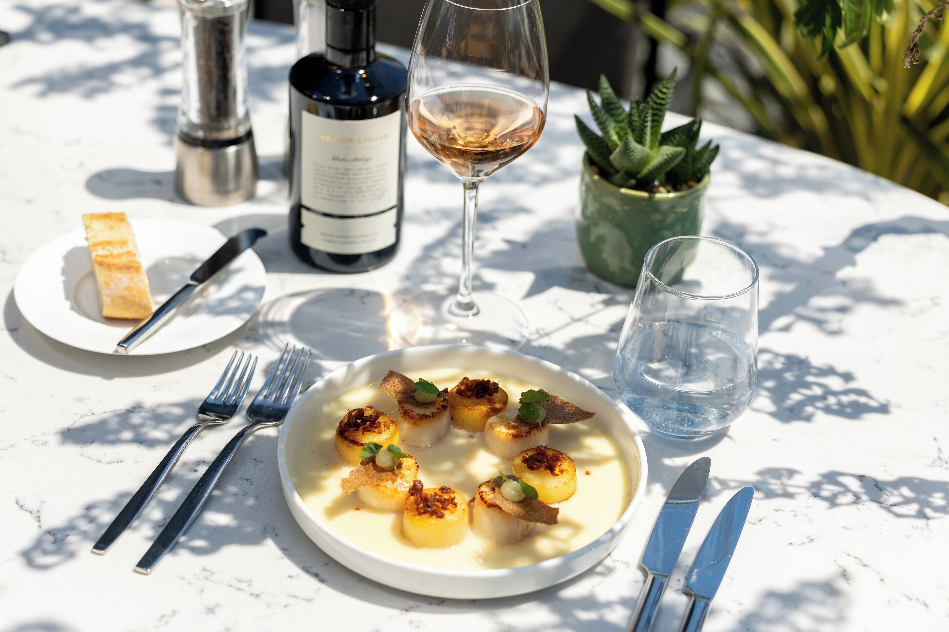 A dining table with a plate of food, a wine bottle, a wine glass, cutlery, and a water glass.