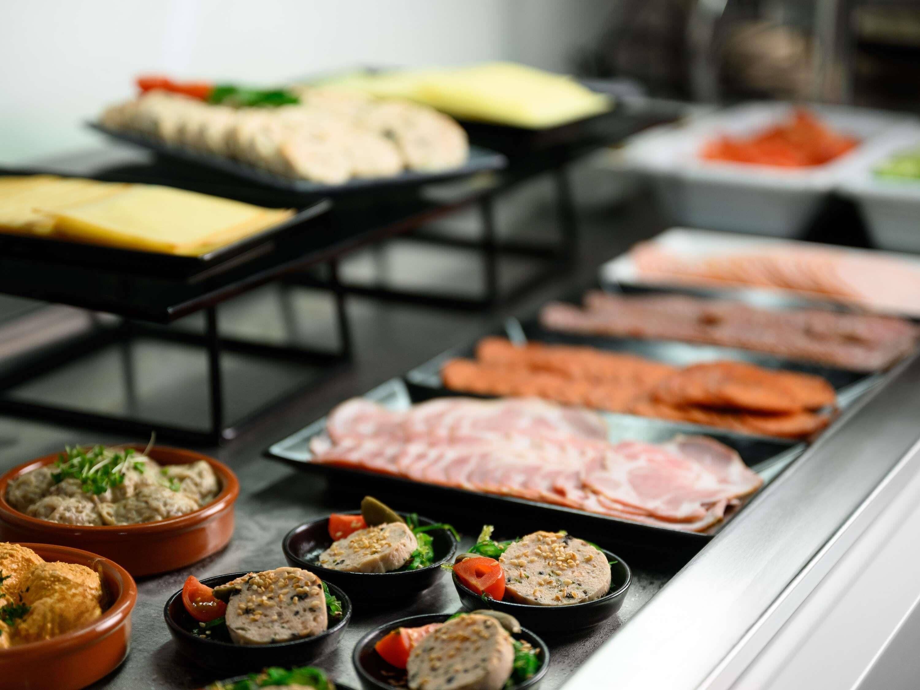 Buffet com diversos alimentos, incluindo carnes, queijos e pratos prontos.
