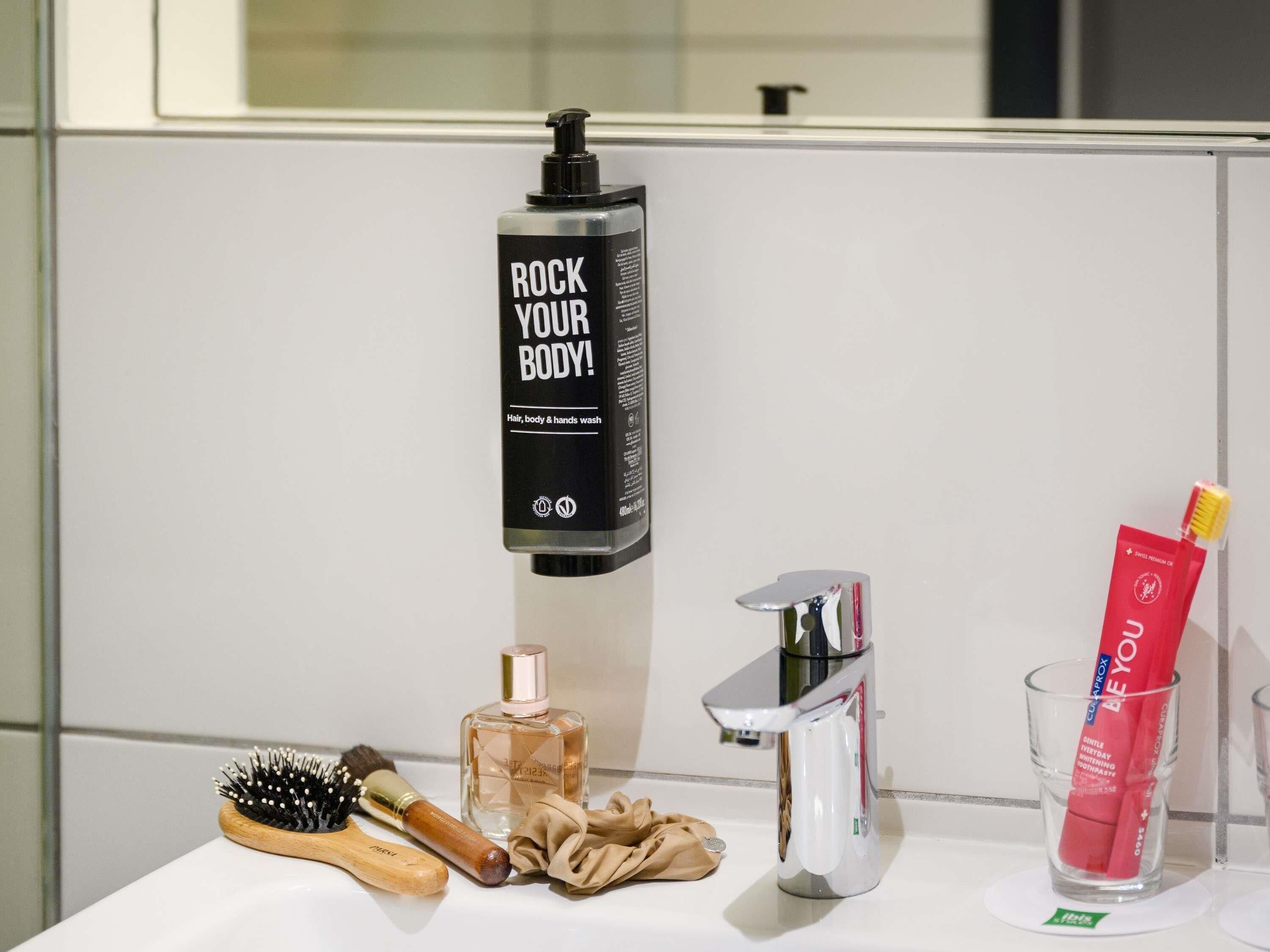 A bathroom with a hand soap dispenser, a hairbrush, a bottle of perfume, a towel, and a toothbrush in a glass.