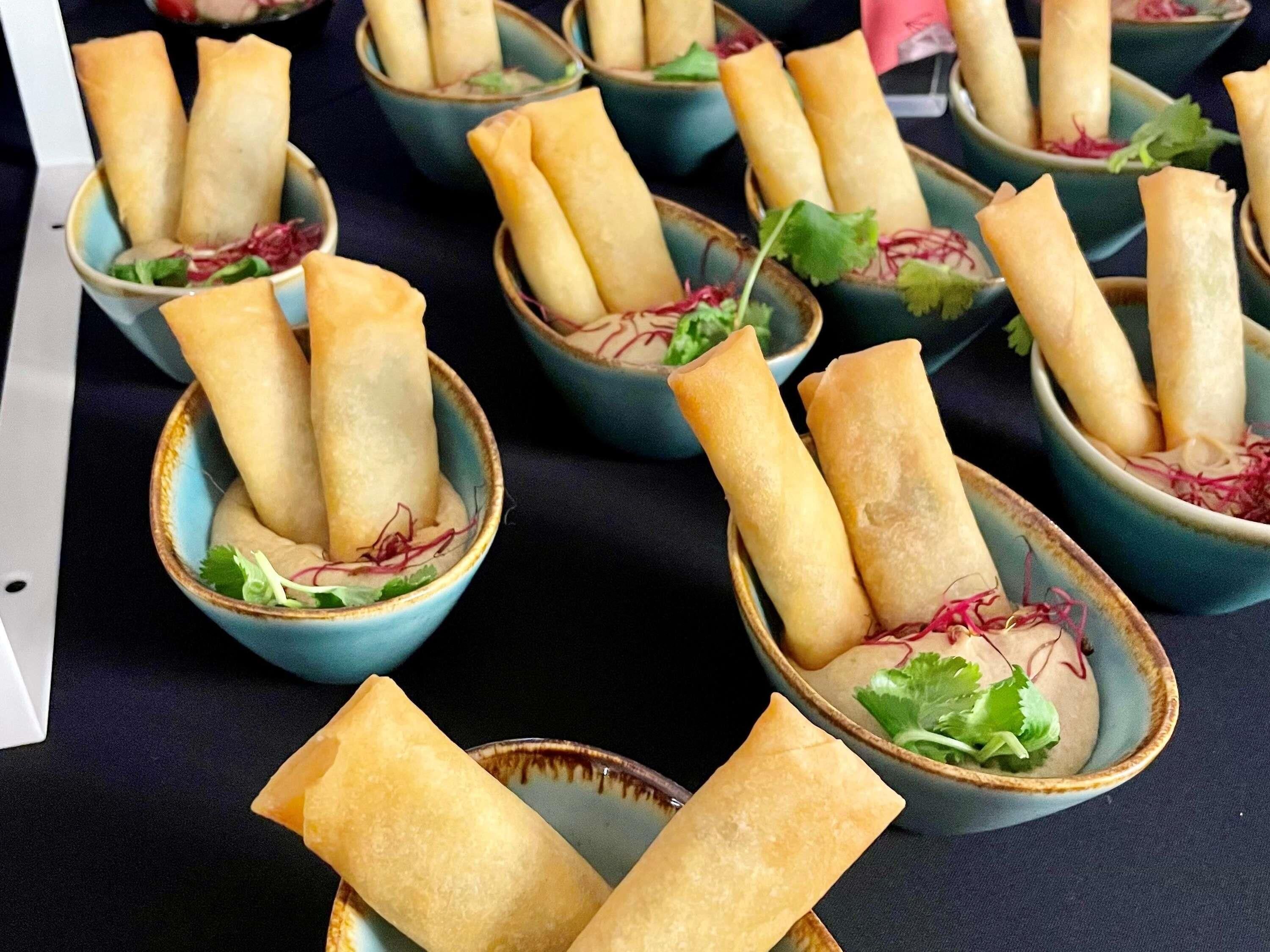 Una mesa con varios cuencos de rollitos de primavera, adornados con hojas verdes.
