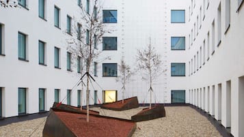 A courtyard with a modern building, trees, and geometric planters.