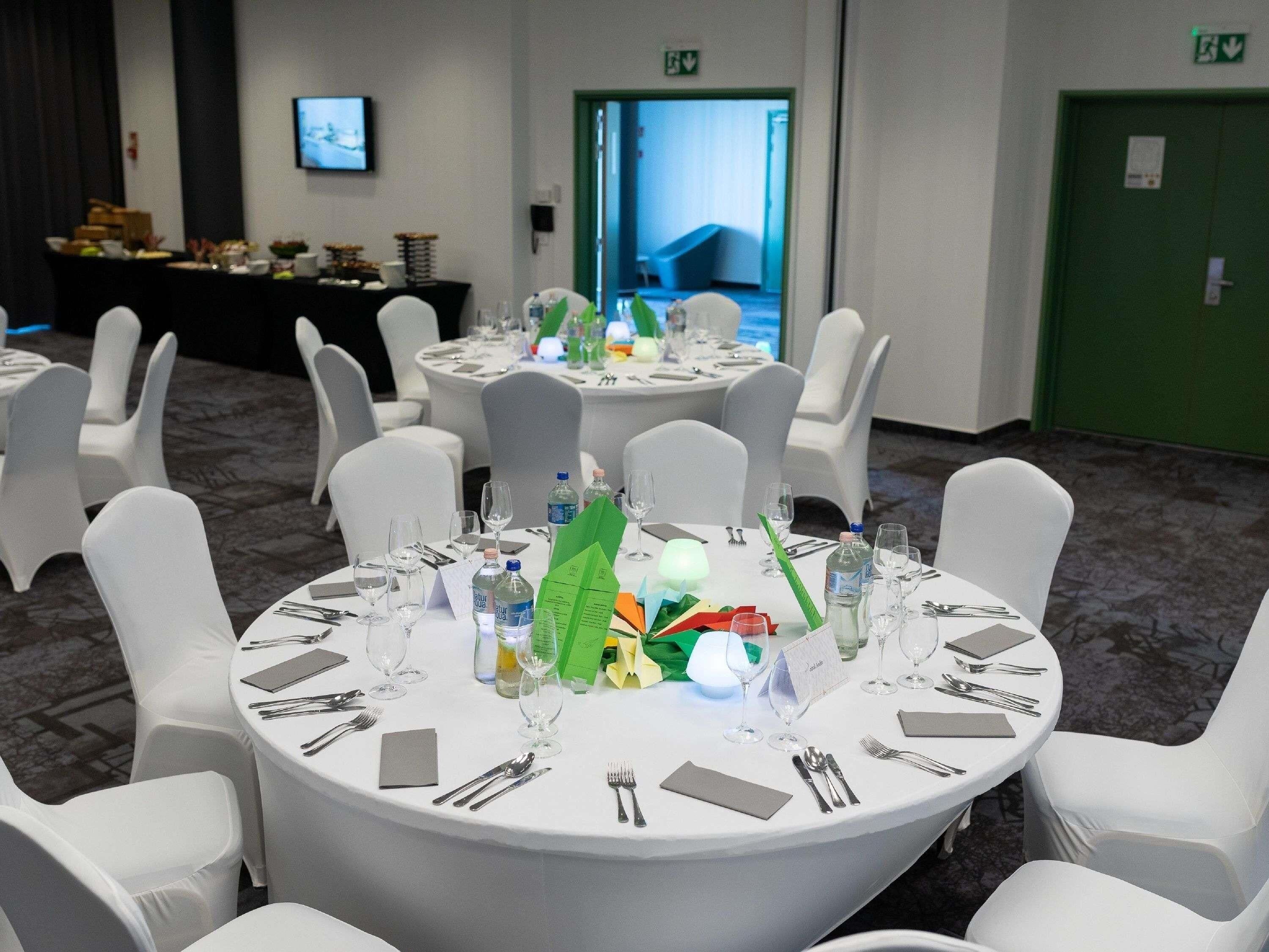 A conference room with round tables, white chairs, and a green exit door.