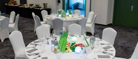 A conference room with round tables, white chairs, and a green exit door.