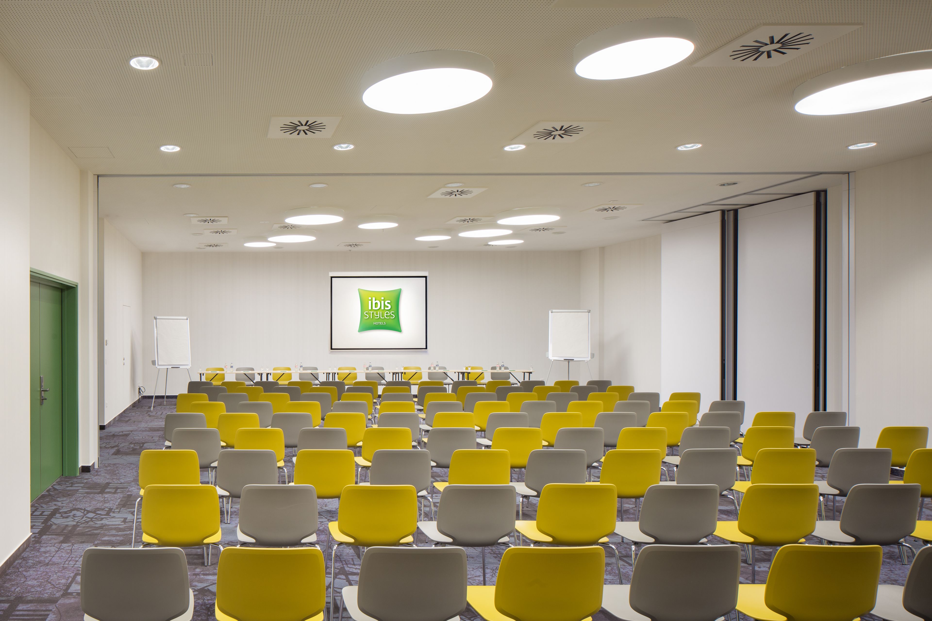 A conference room with rows of chairs, a whiteboard, and a projector screen displaying "ibis Styles".