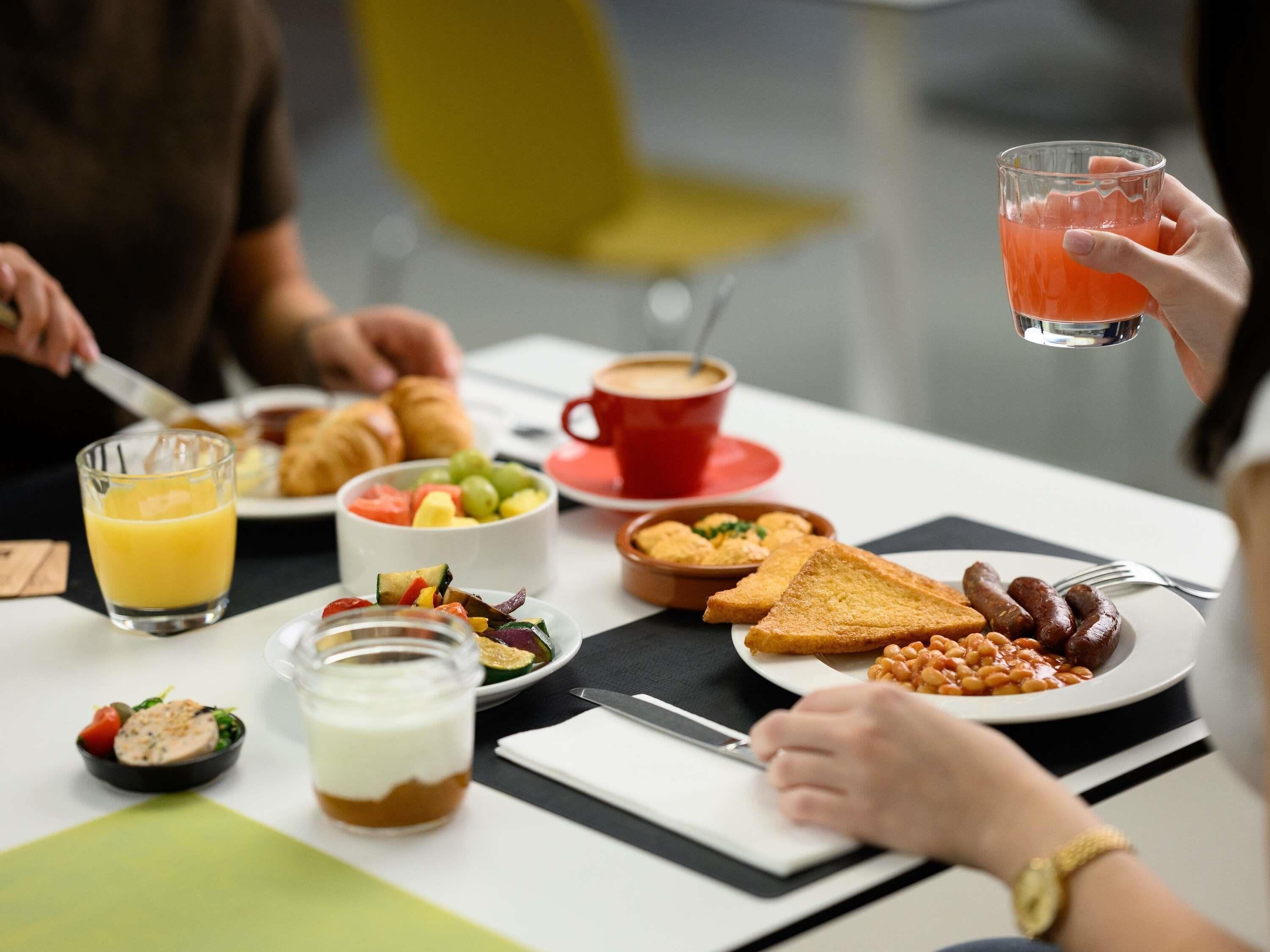 Desayuno con diversos platos, incluyendo tostadas, salchichas, frijoles y una ensalada de frutas.