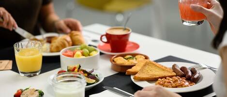 Desayuno con diversos platos, incluyendo tostadas, salchichas, frijoles y una ensalada de frutas.