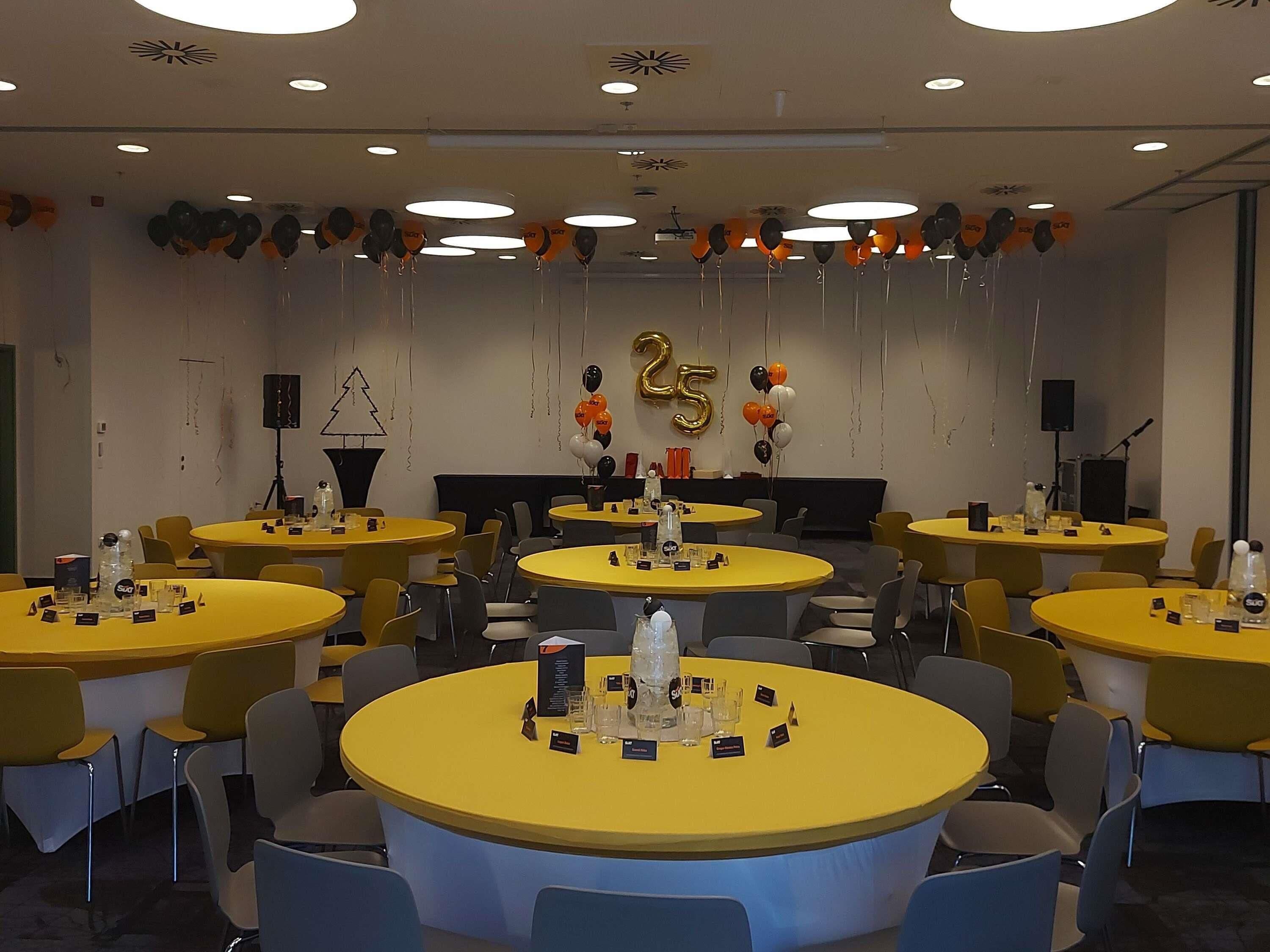 Un salón de conferencias con varias mesas, sillas y un escenario decorado con globos.