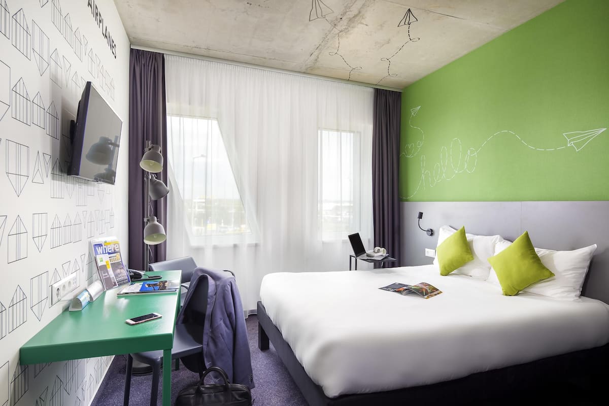 Een hotelkamer met een bed, bureau en een televisie aan de muur.