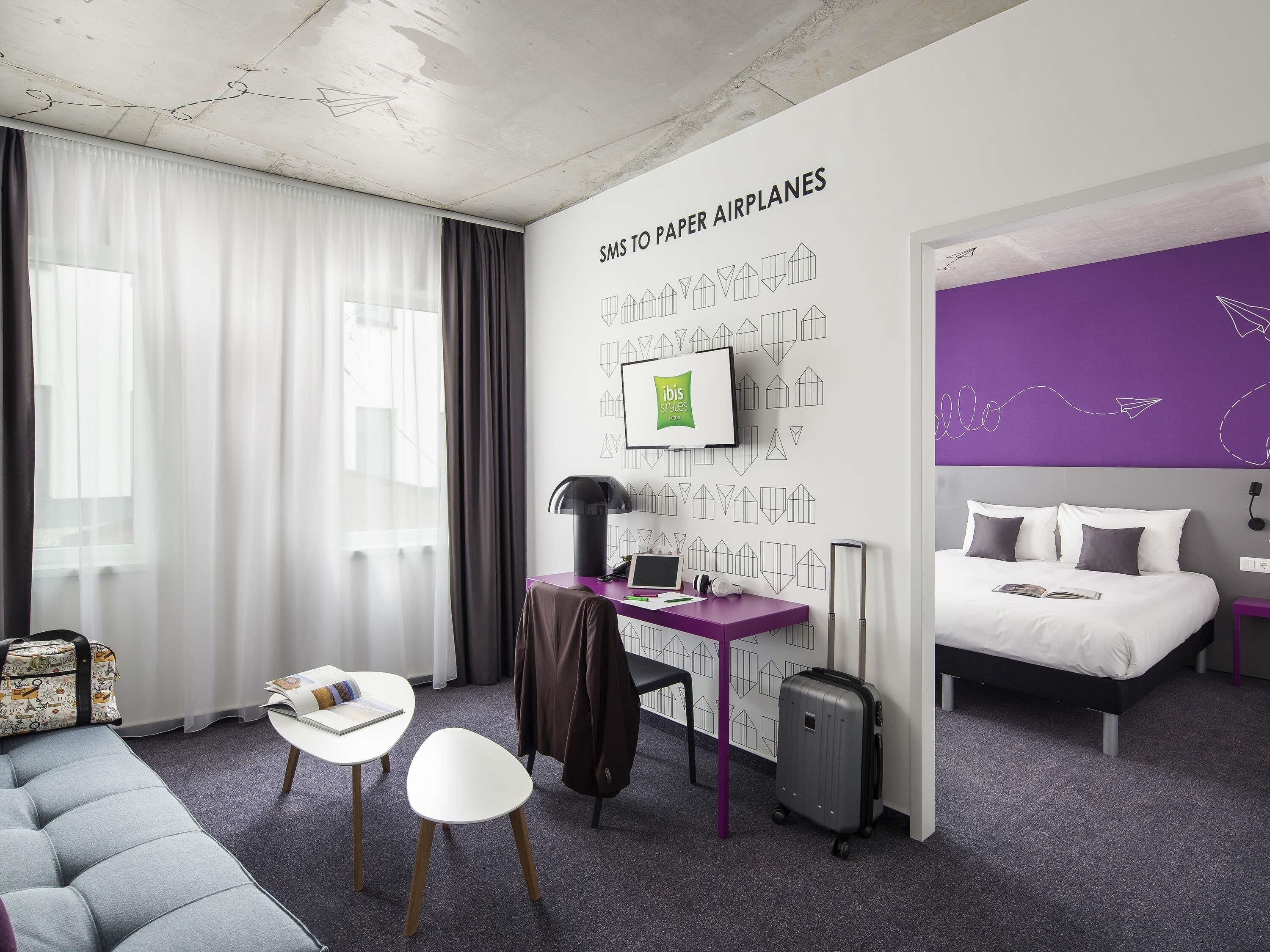 Ein Hotelzimmer mit Bett, Schreibtisch, Stuhl und einer Wand mit geometrischem Muster.
