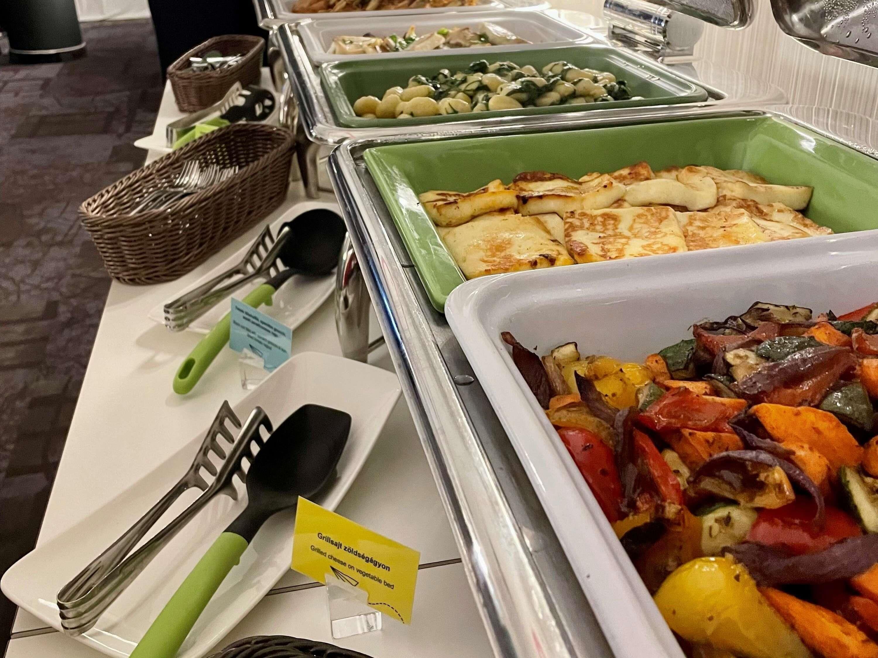Un buffet proposant divers plats, notamment des croque-monsieur servis sur un lit de légumes, ainsi que des ustensiles tels que des pinces et une spatule.