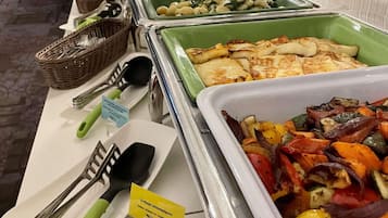Un bufé con diversos platos, incluyendo queso a la plancha sobre una cama de vegetales, y utensilios como pinzas y una espátula.