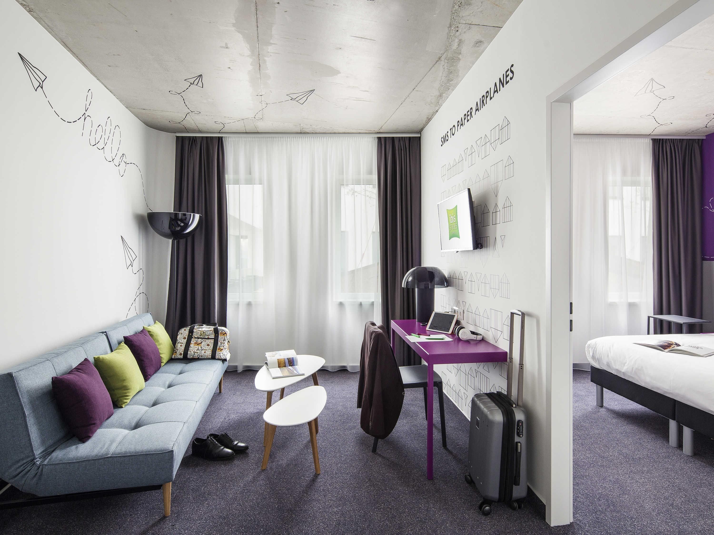 Une chambre d’hôtel moderne équipée d’un canapé, d’un bureau, d’un lit et d’une valise.