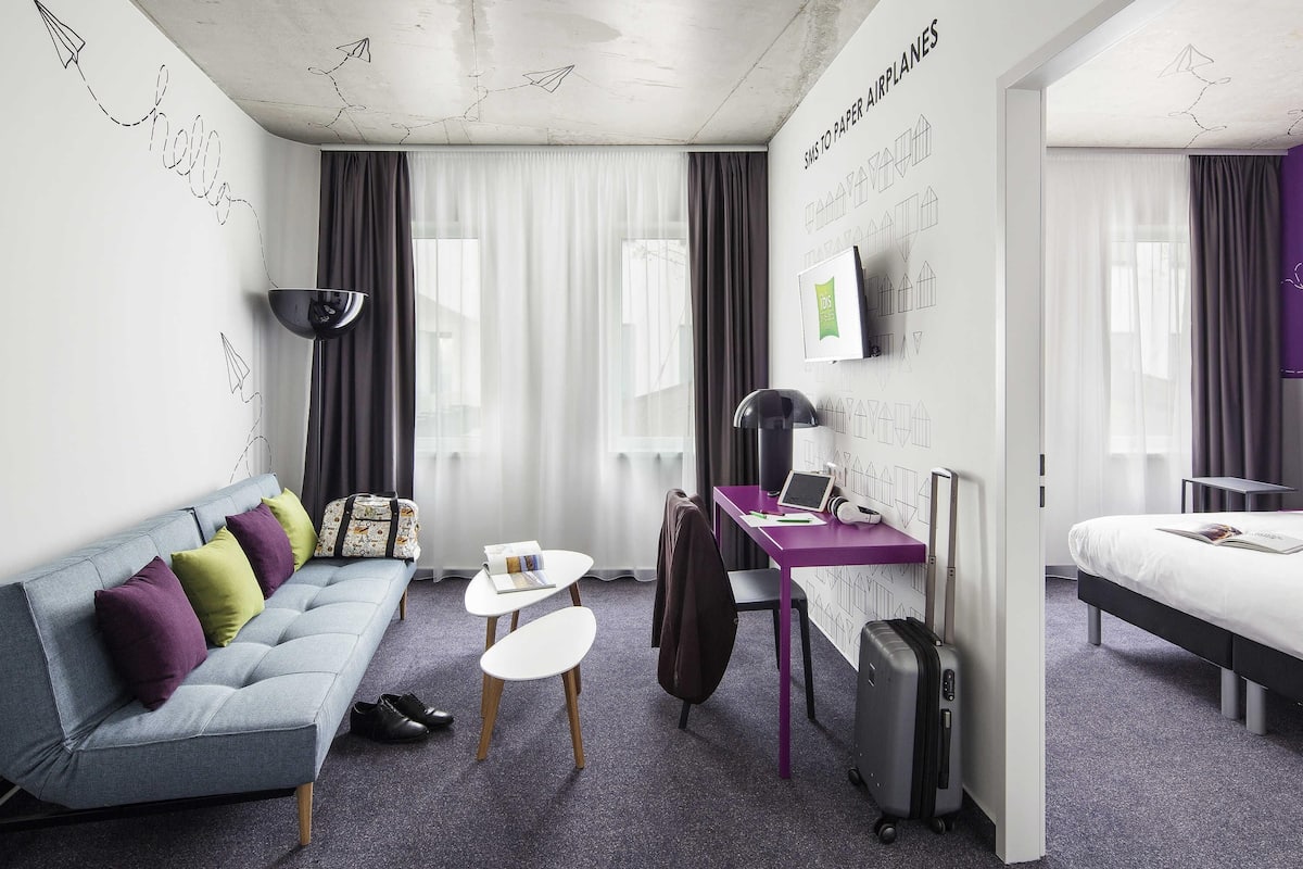 Une chambre d’hôtel moderne équipée d’un canapé, d’un bureau, d’un lit et d’une valise.