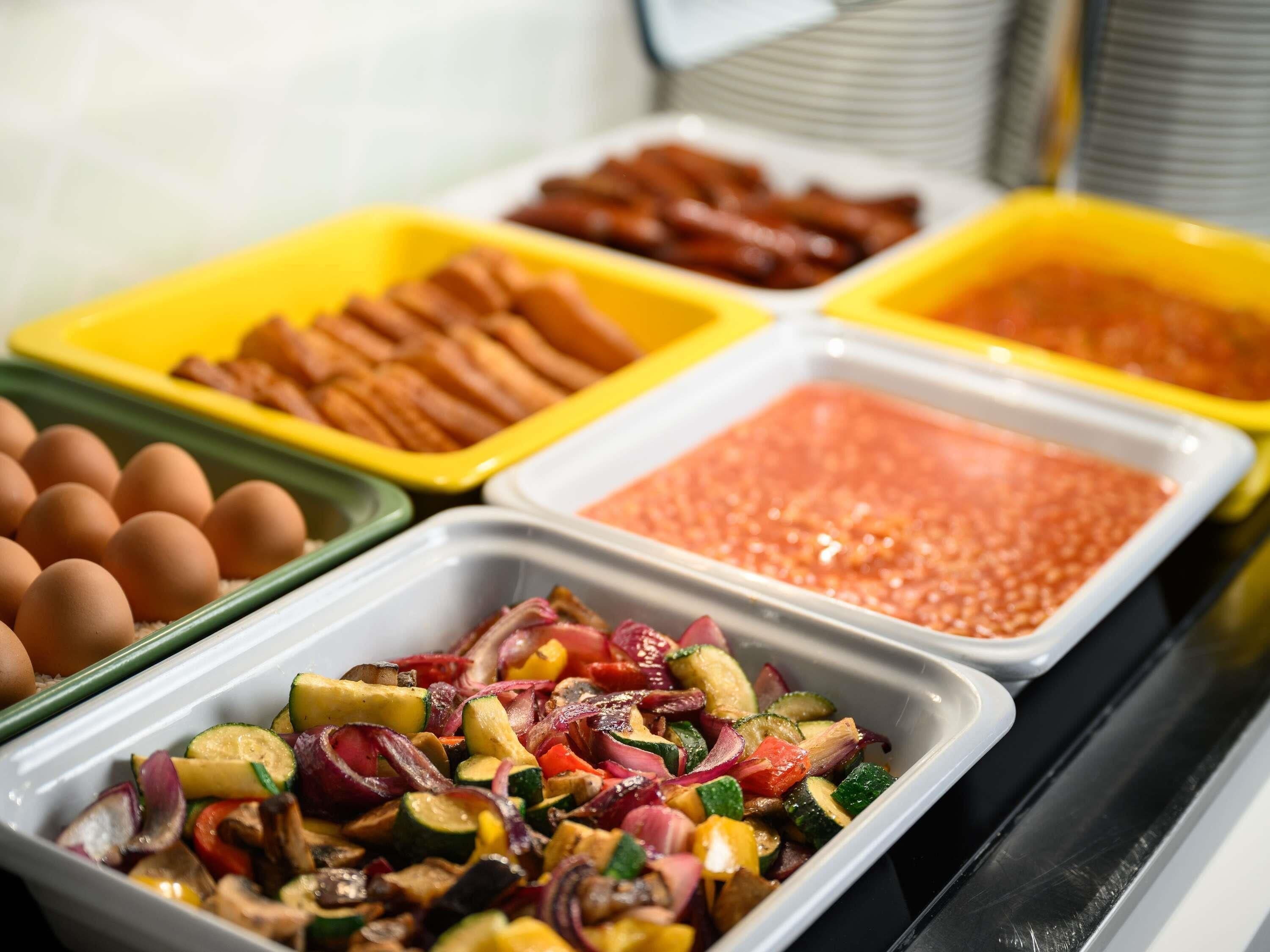 Buffet com diversas opções de comida, incluindo ovos, salsichas e um prato de legumes.