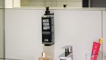 A bathroom sink with a bottle of body wash, a brush, a glass of mouthwash, and a towel.