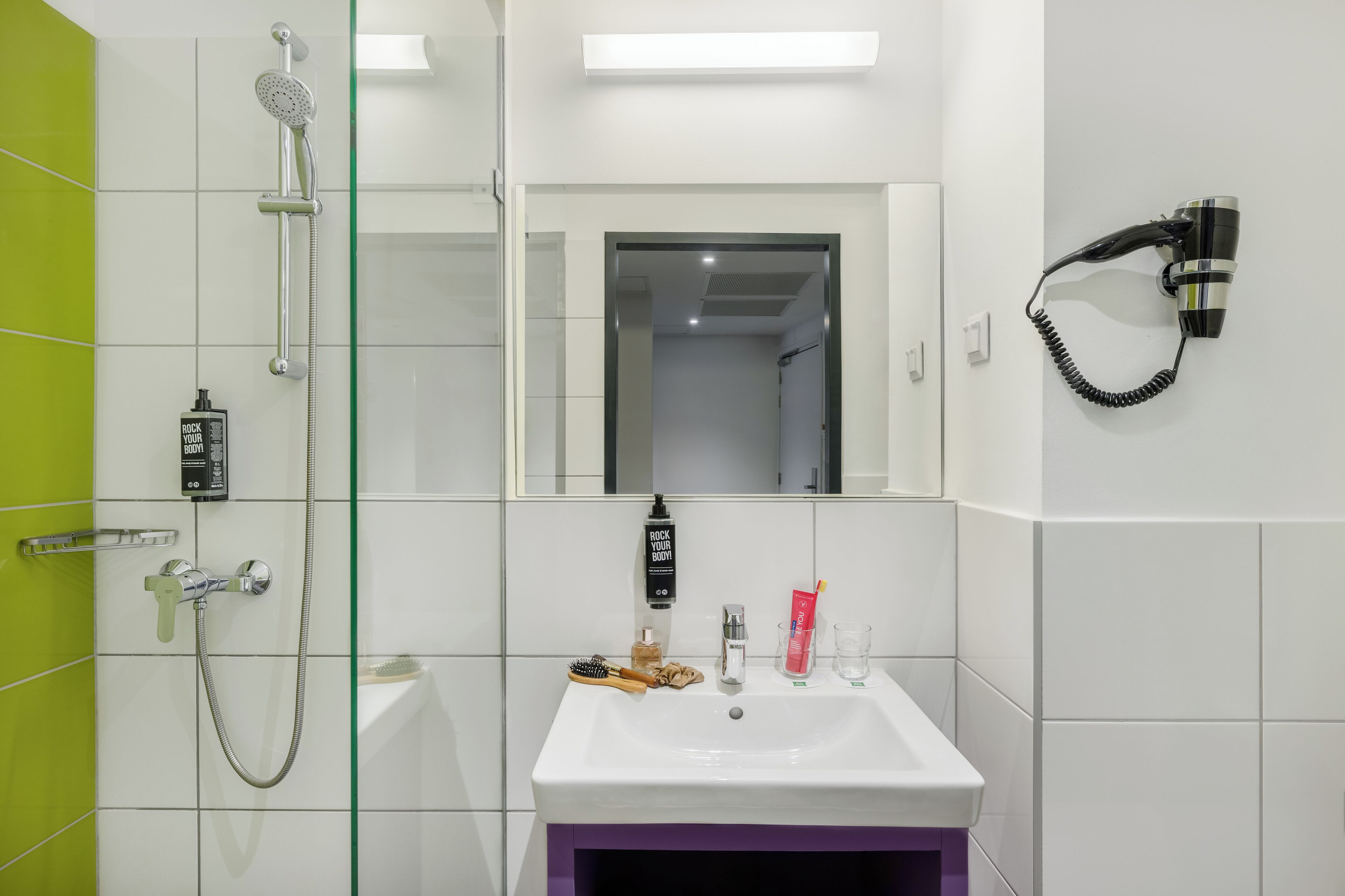 Un bagno con doccia, lavandino, specchio e asciugacapelli fissato al muro.