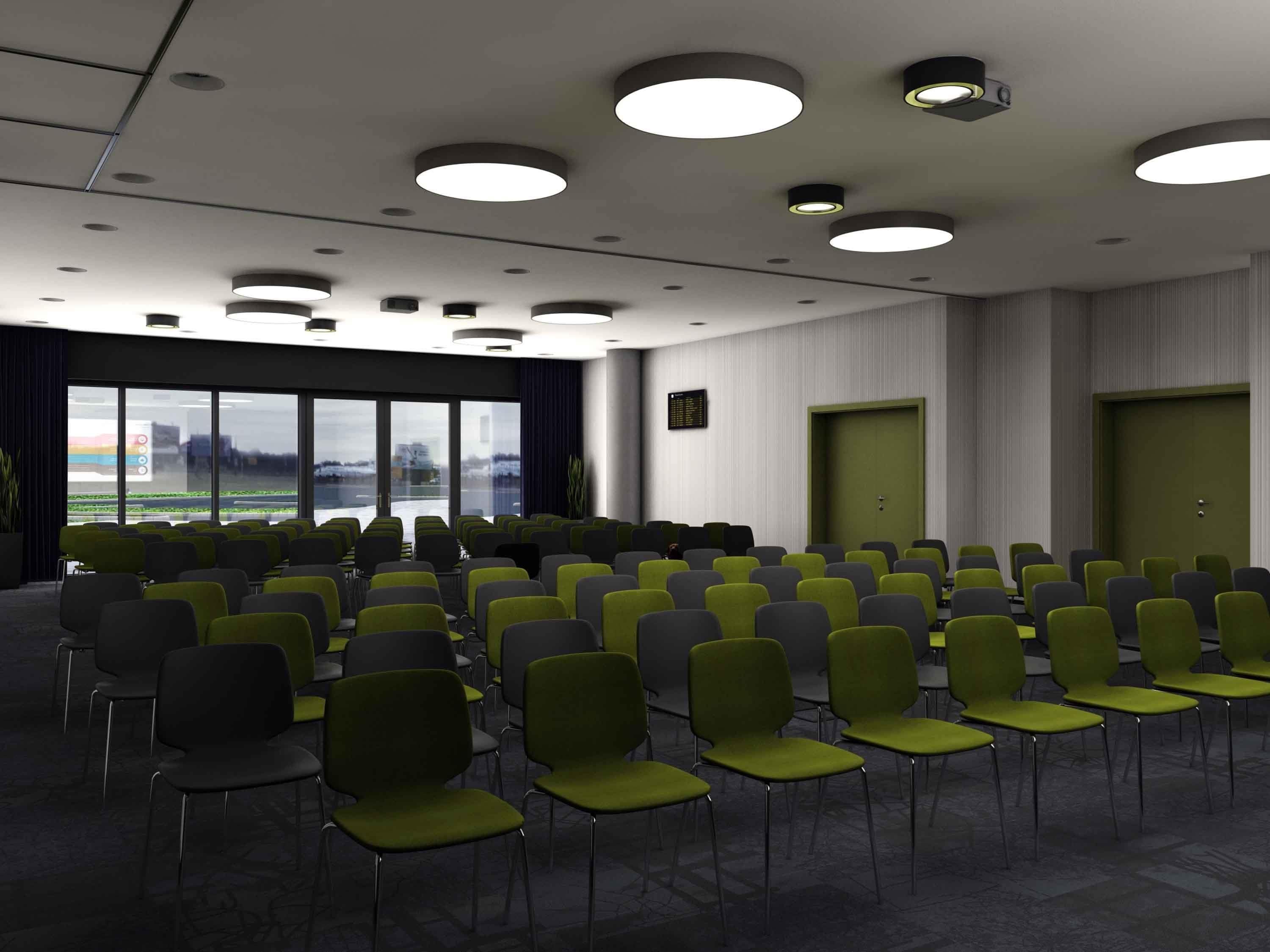 Un salón de conferencias con filas de sillas, ventanas amplias y una puerta verde.
