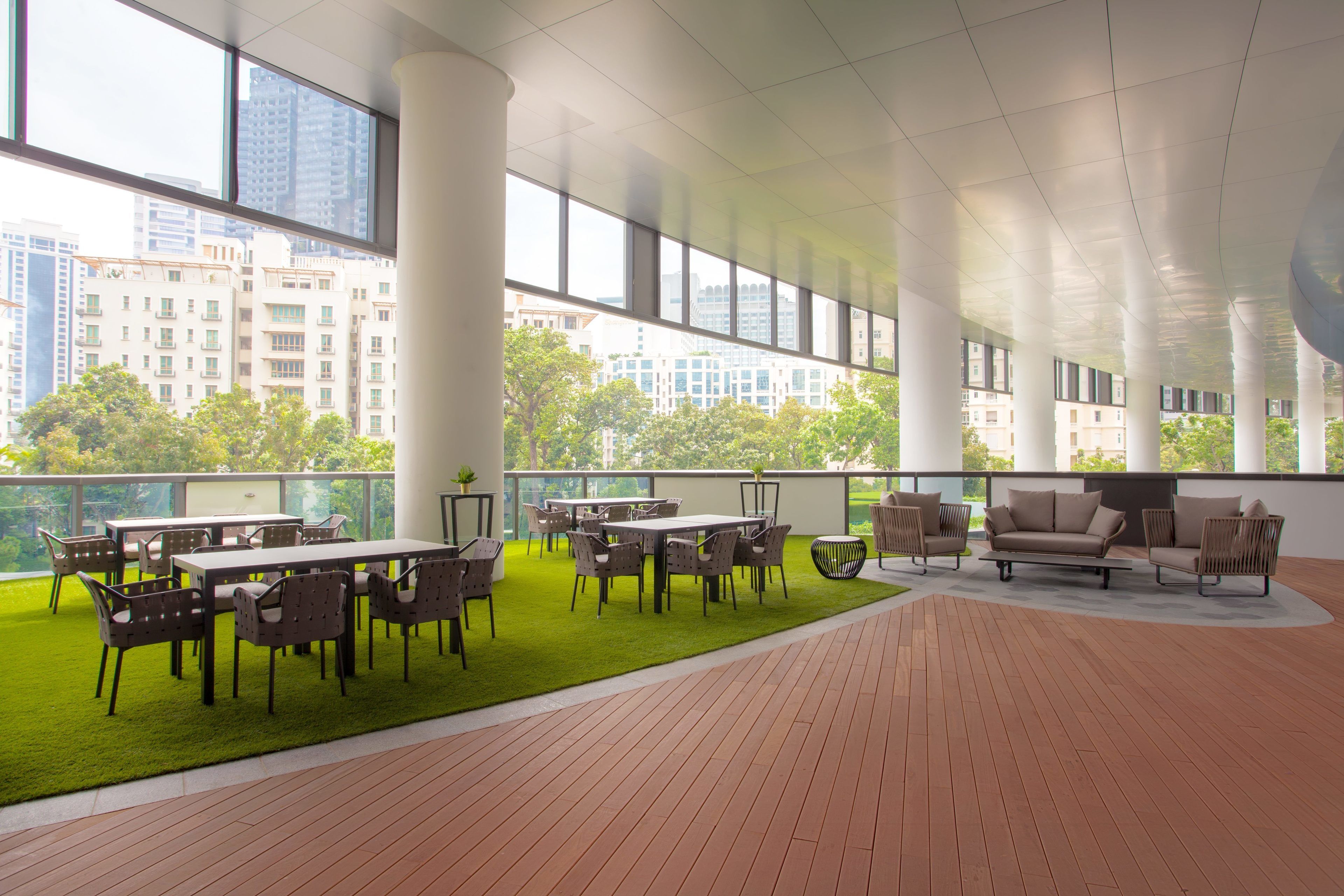 Un espacio interior amplio con césped artificial verde, una terraza de madera y un área de descanso con mesas y sillas.