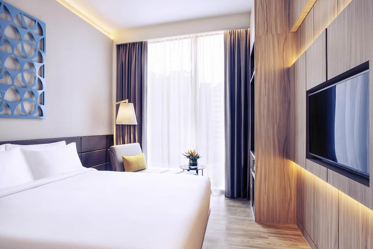 Hotellihuone, jossa on suuri sänky, televisio, lamppu ja koristeellinen seinäelementti.