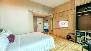 A hotel room with a bed, a TV on the wall, a wooden wardrobe, and a small table with a remote control.