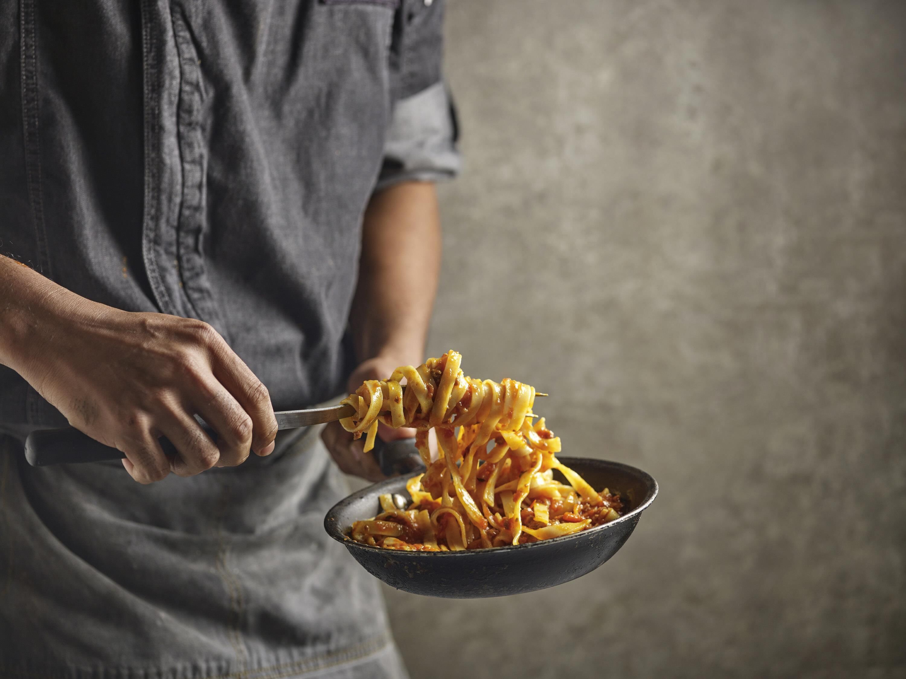 A person holding a pan of spaghetti.