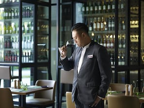 A man in a suit holding a wine glass in a bar with shelves of bottles.