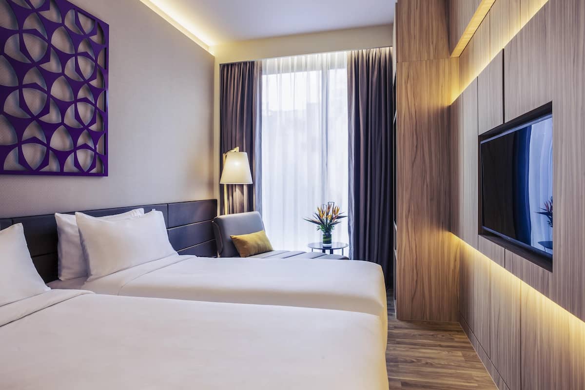 Quarto de hotel com duas camas, televisão na parede, abajur e um painel decorativo.