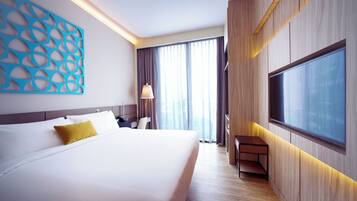 A modern hotel room with a large bed, a desk, a TV, and a view of the city through large windows.