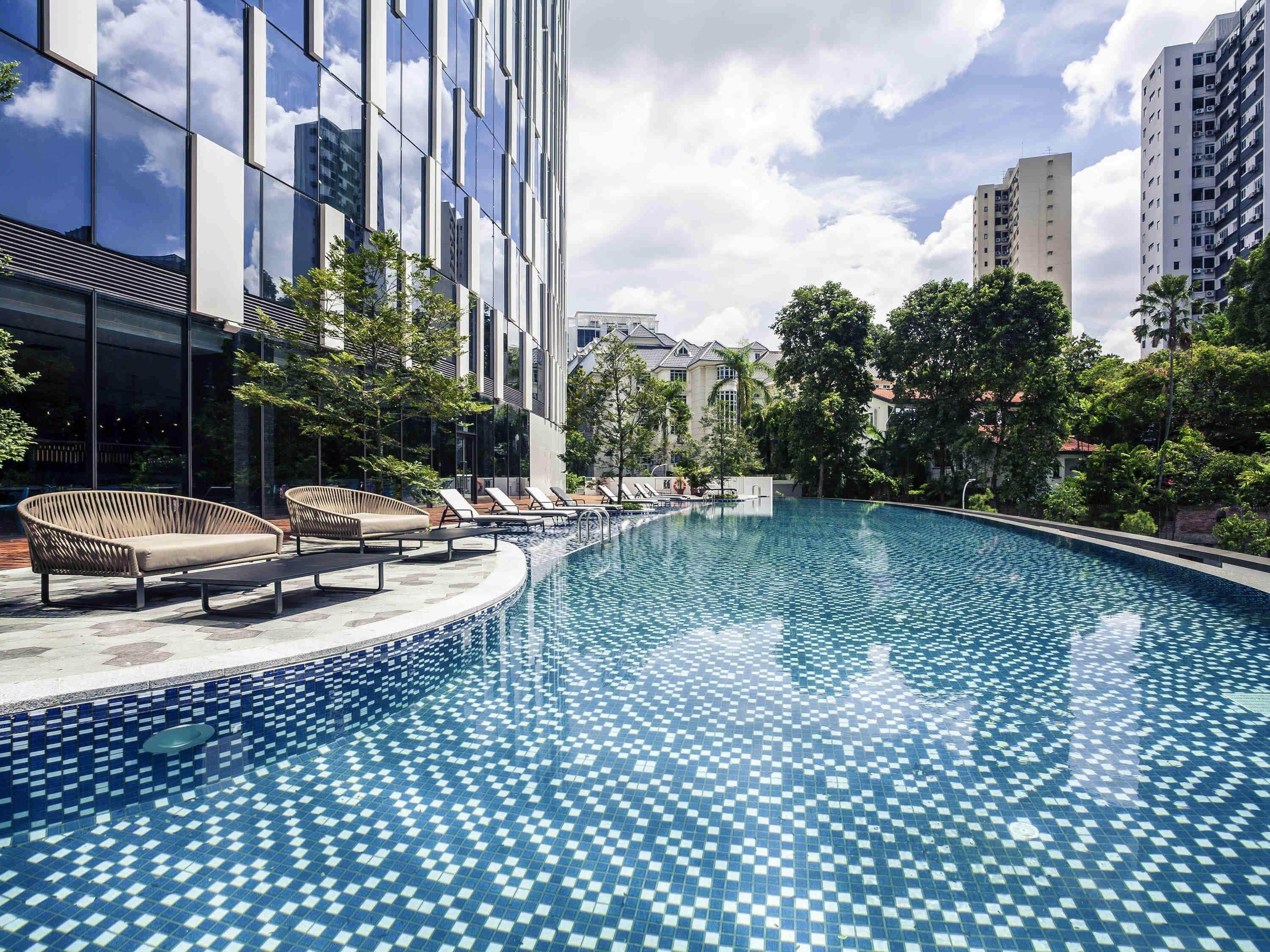 Un hôtel moderne doté d’une grande piscine extérieure, de chaises longues et d’un jardin bien entretenu.