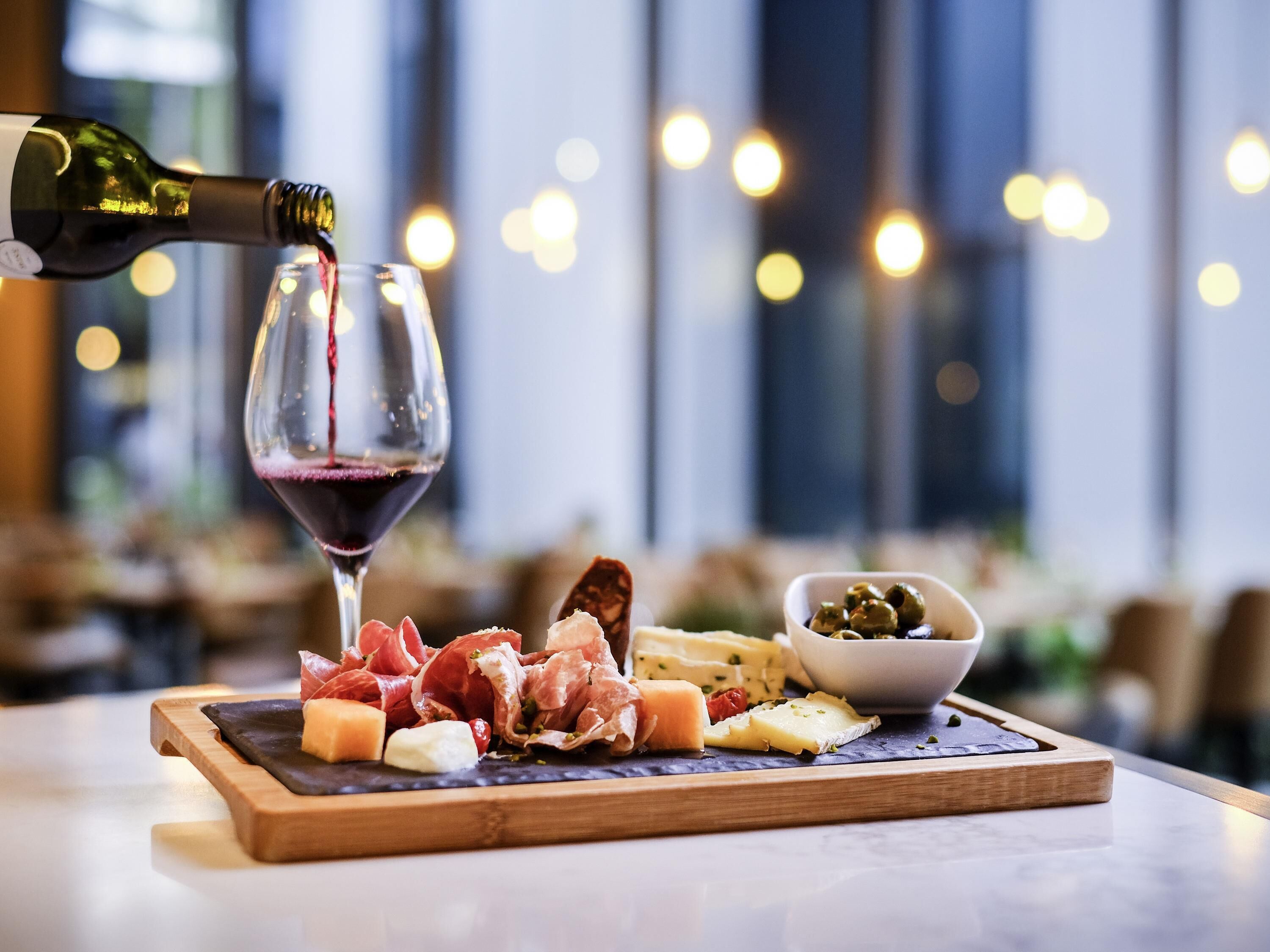 Eine Wurst- und Käseplatte mit verschiedenen Sorten, ein Glas Rotwein und eine Oliven-Schale.