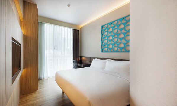 A hotel room with a large bed, a desk, a chair, a TV, and a window with curtains.