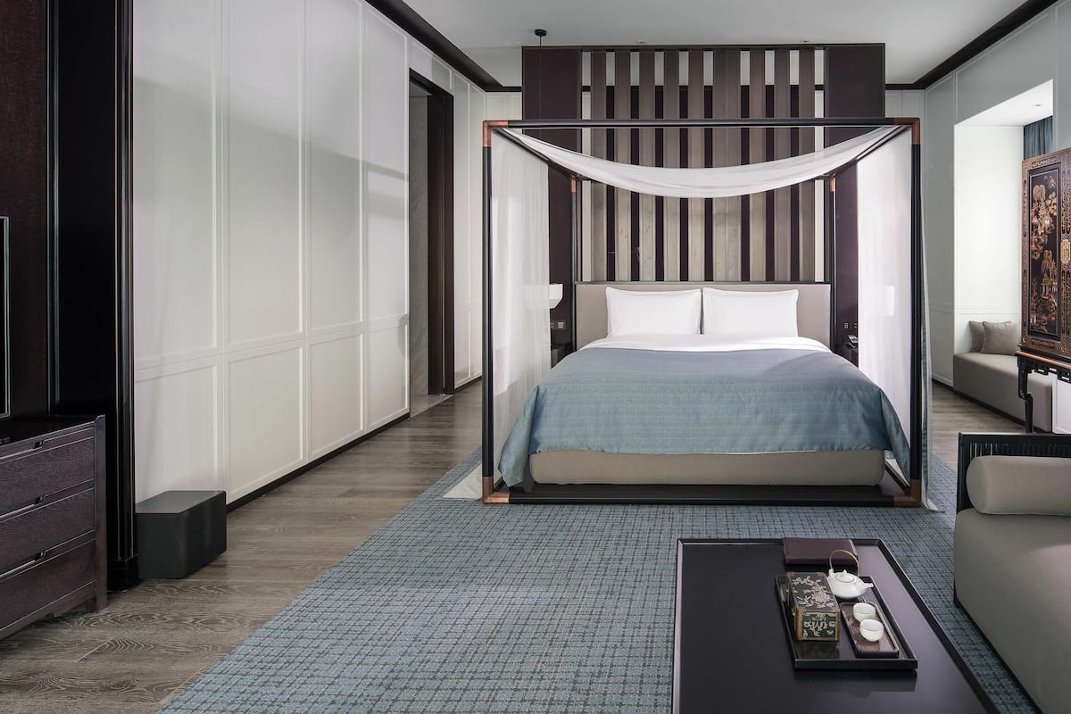 A modern bedroom with a canopy bed, a flat-screen TV, a sofa, and a tray with teapot and cups.