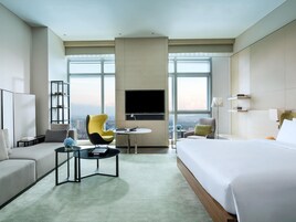 Habitación de hotel con una cama grande, un sofá, una silla, una mesita, un televisor y vistas a la ciudad.