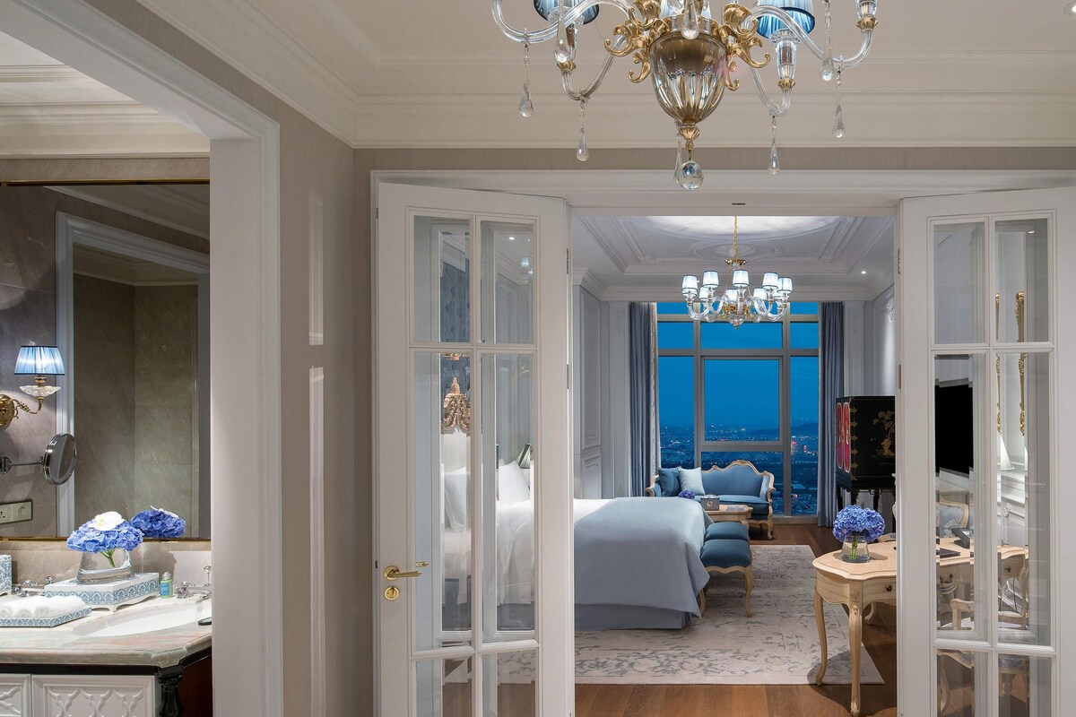 Ein luxuriöses Schlafzimmer mit einem großen Bett, einer Sitzecke und Blick auf die Stadt.