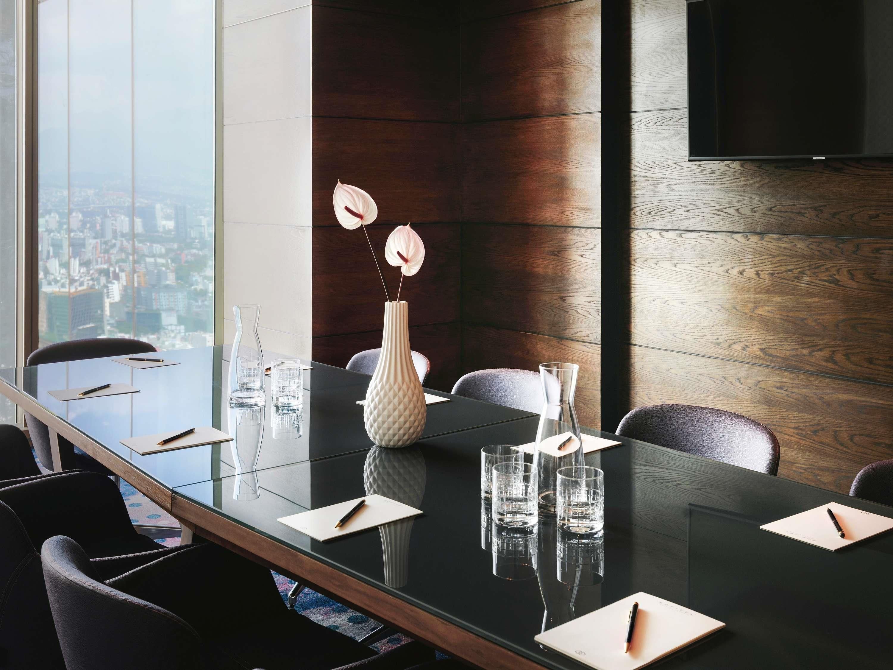 A conference room with a glass table, chairs, a vase with flowers, and a city view.
