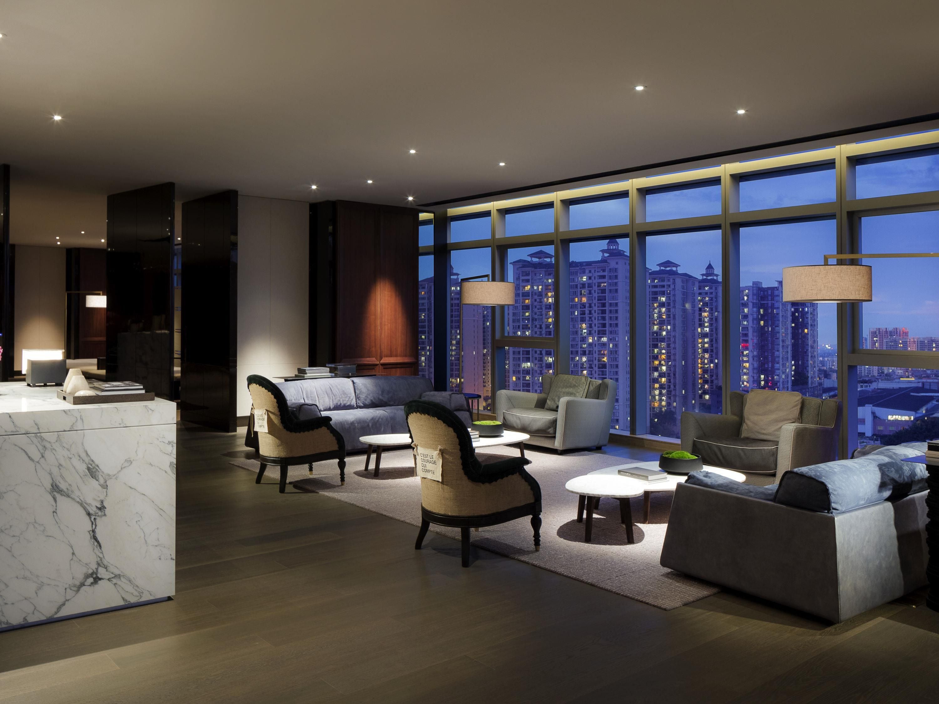 A modern hotel lobby with a marble reception desk, comfortable seating, and large windows offering a city view.