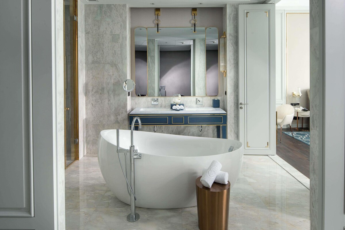 Ein modernes Badezimmer mit einer freistehenden Badewanne, einem Waschtisch mit Spiegel und einer Tür zu einem weiteren Raum.