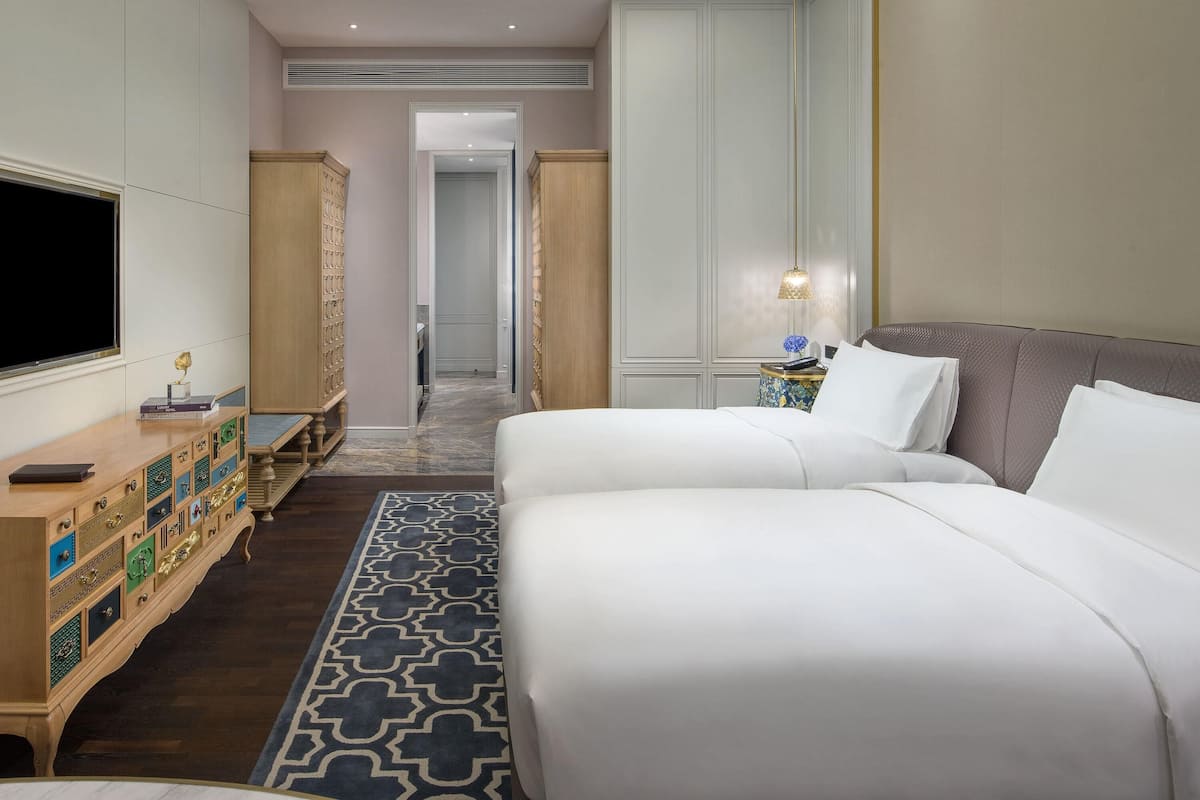 A hotel room with a large bed, a TV, a desk with drawers, a nightstand, and a patterned rug.