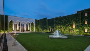 Une cour avec une fontaine, des colonnes blanches et un bâtiment dont le mur est recouvert de lierre.